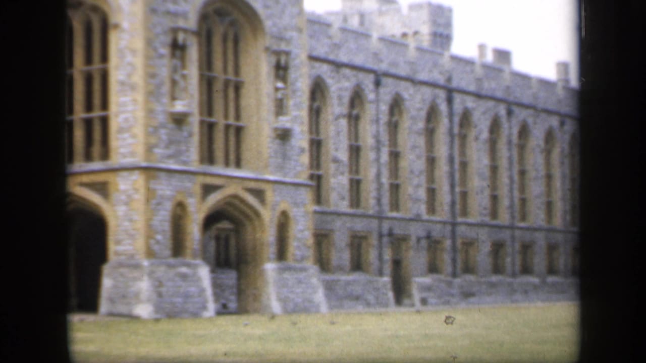 1949 England frame showing a long castellated stone exterior with repeated arched windows and clipped lawn below.