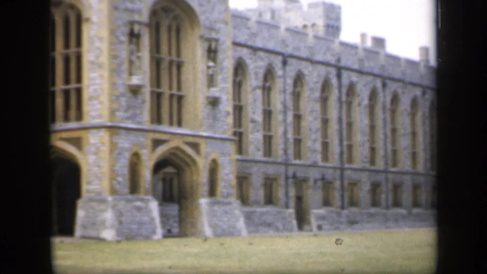 1949 England frame showing a long castellated stone exterior with repeated arched windows and clipped lawn below.