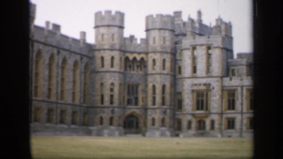 Wider 1949 England frame of a Gothic-style stone building with towers, arched windows, crenellations, and lawn.