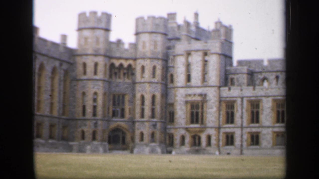 1949 England 8mm view of a large grey stone castle facade with crenelated towers, arched entrance, brown-framed windows, and lawn.