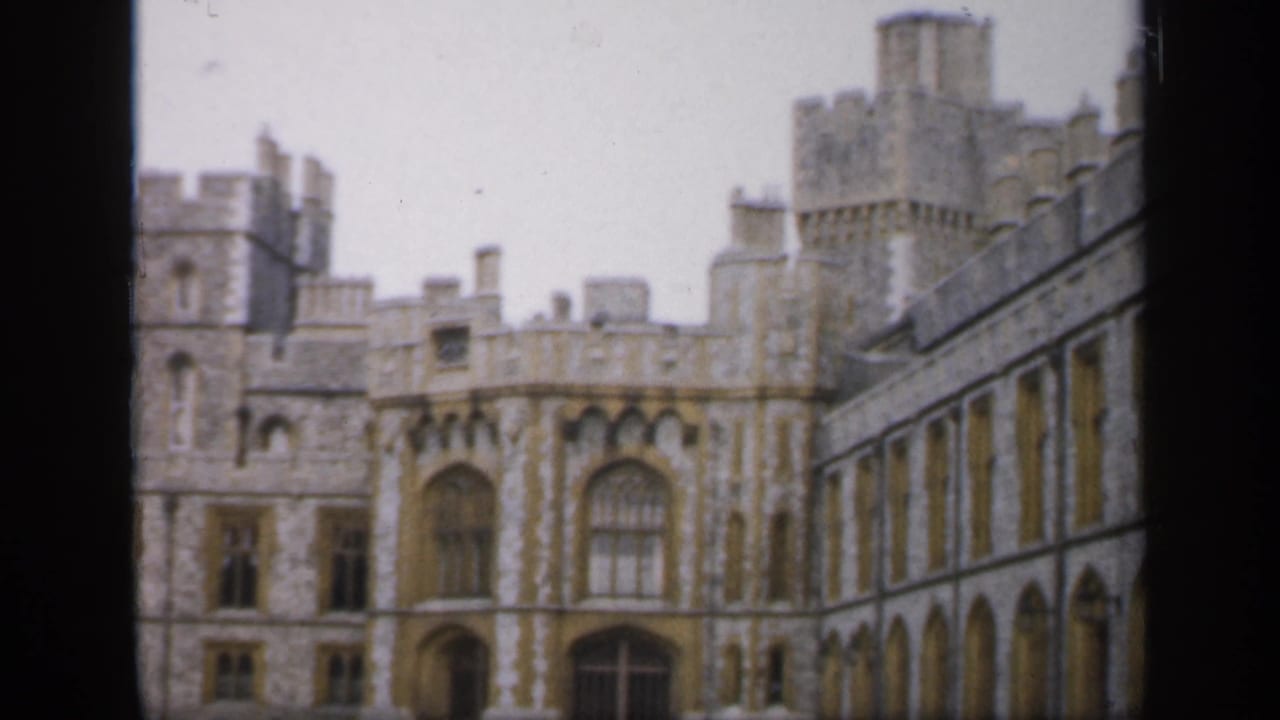 1949 England 8mm frame of a historic castle exterior, including tower forms, arched windows, and a long stone wing at right.