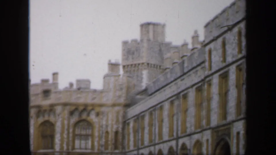 1949 England 8mm frame with motion-softened castle architecture, showing a tower, arched window, and long stone wall.