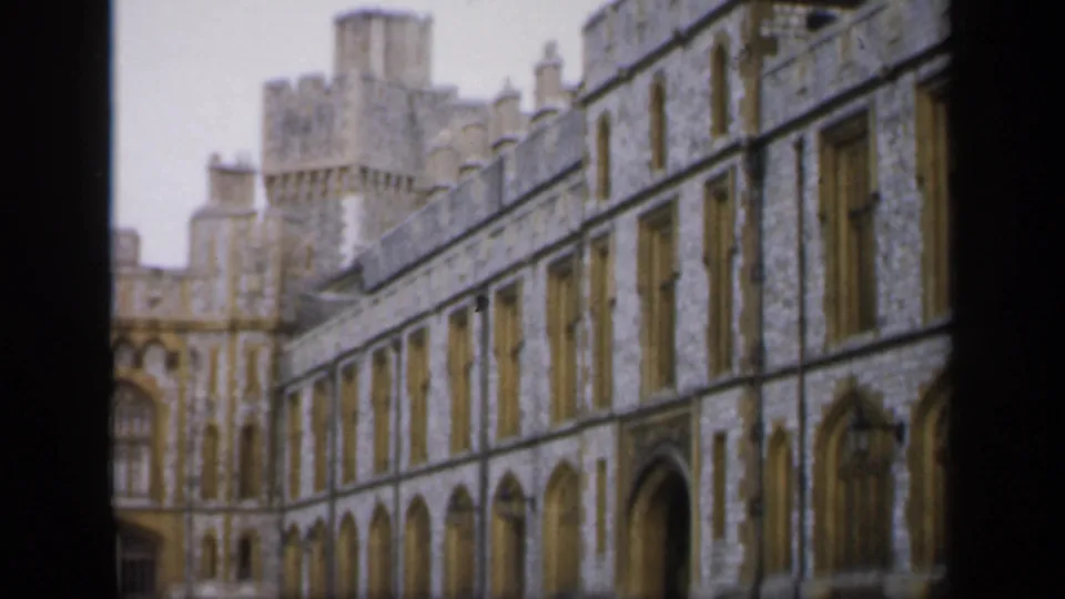 1949 England 8mm frame showing a long castle wing with repeated Gothic-style arches and a tower rising behind the roofline.