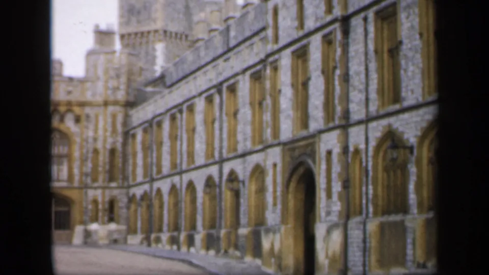 1949 England home-movie frame showing a stone castle facade with Gothic arches, tall windows, and dark film borders.