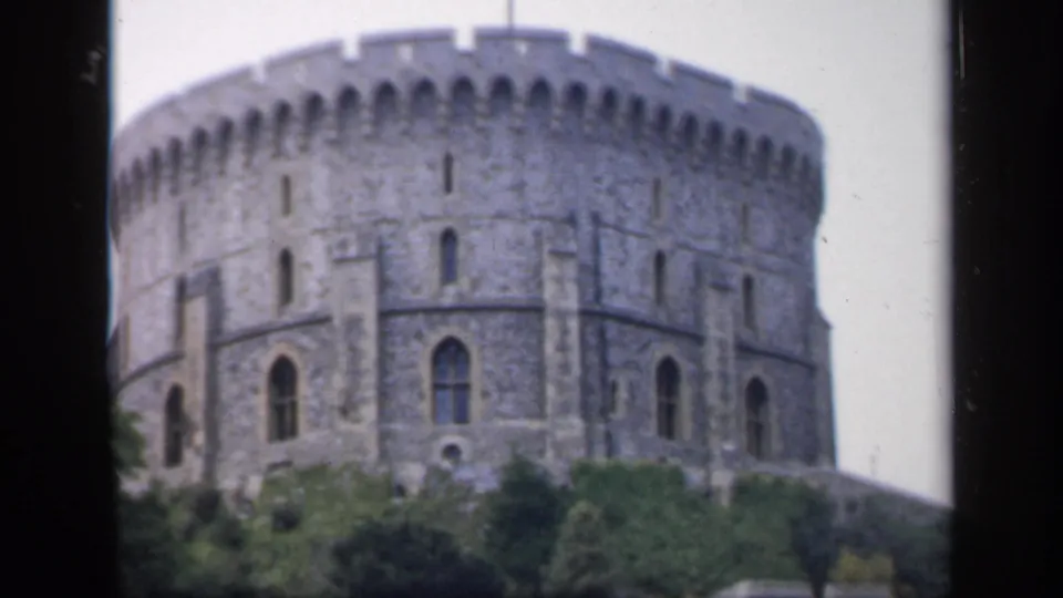 1949 England 8mm frame of a round stone tower with arched windows, crenellated top, and soft-focus greenery below.