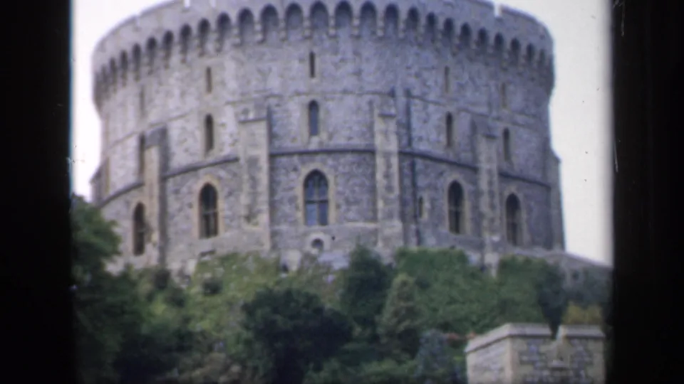 1949 England home-movie frame showing the round stone castle tower from a slightly wider angle with trees and film borders visible.
