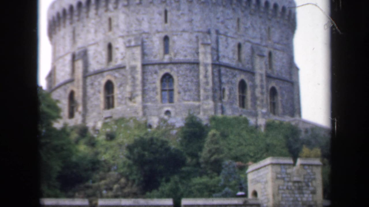 Grey stone round castle tower above trees and a low wall.