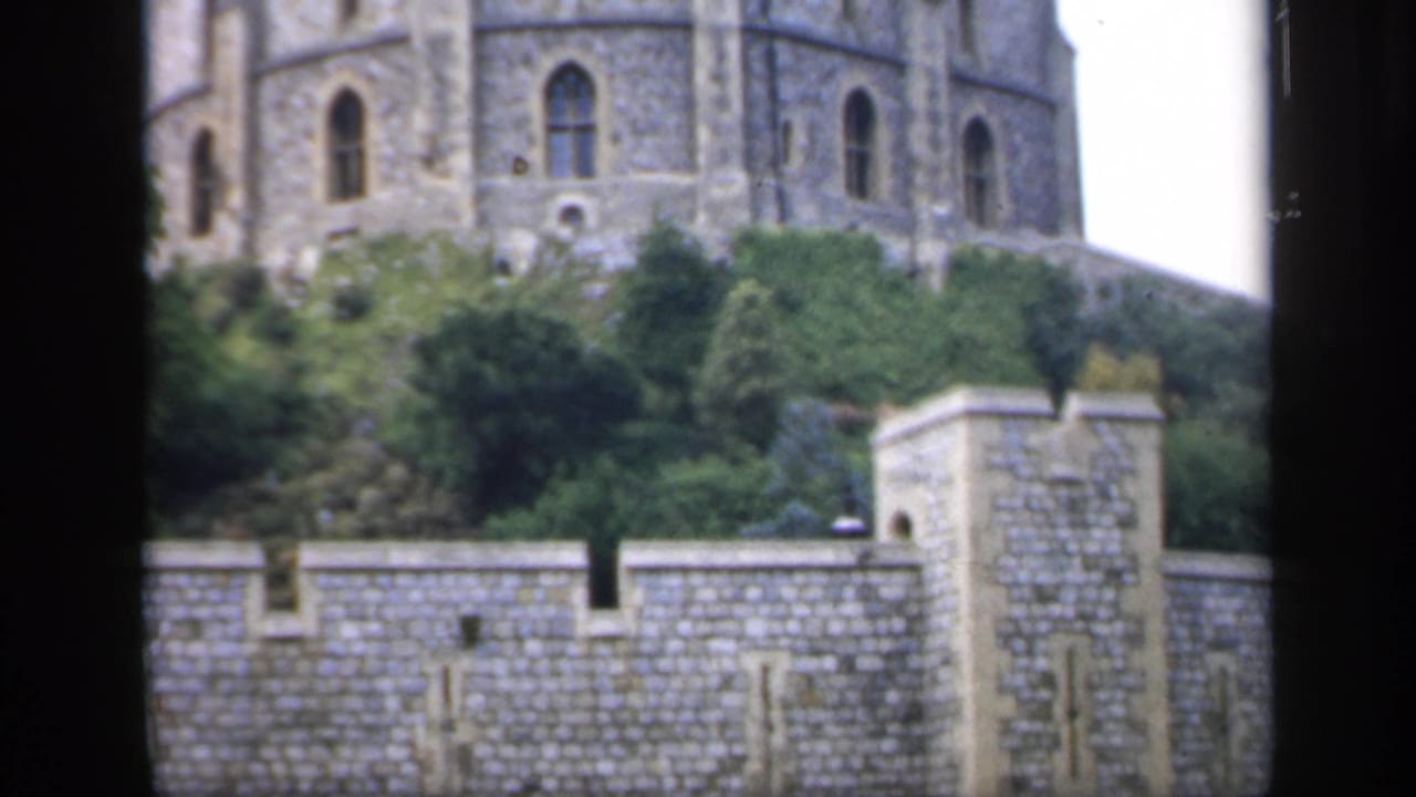 Stone castle wall and tower with trees on a raised embankment.