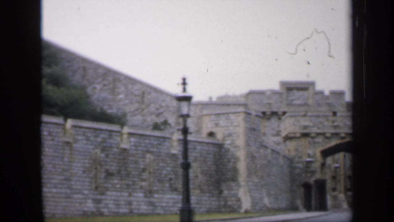 1949 England 8mm frame with stone walls, a foreground lamppost, crenellated masonry, and part of an arched gateway.