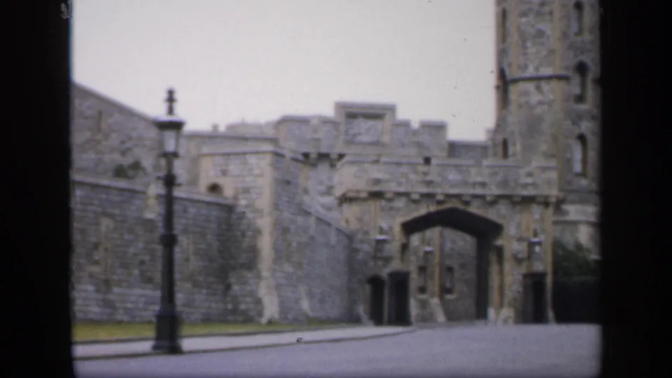 1949 England 8mm frame centered on an arched stone gateway with tower masonry, road, lamppost, and low walls.