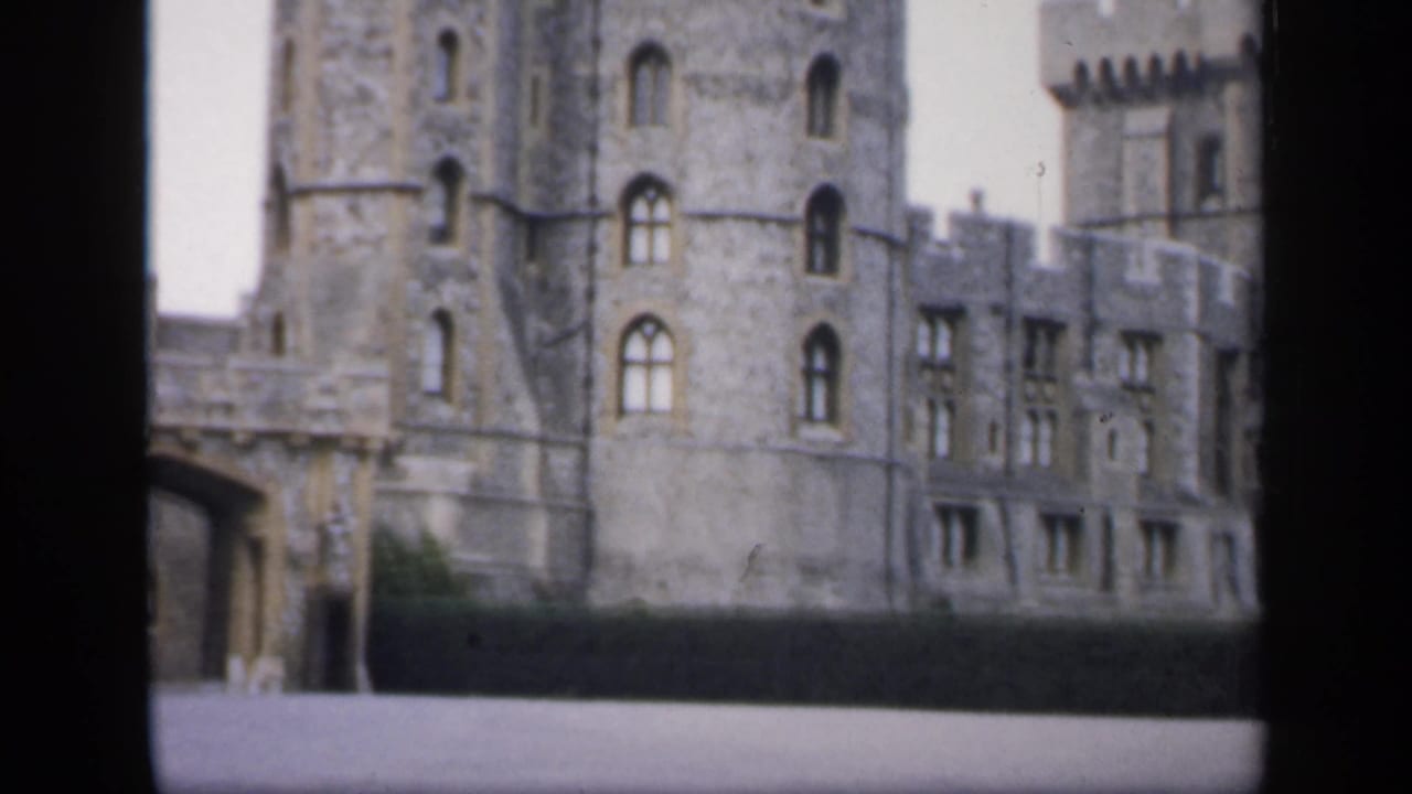 Grey stone castle towers and arched windows seen beyond a dark foreground wall.