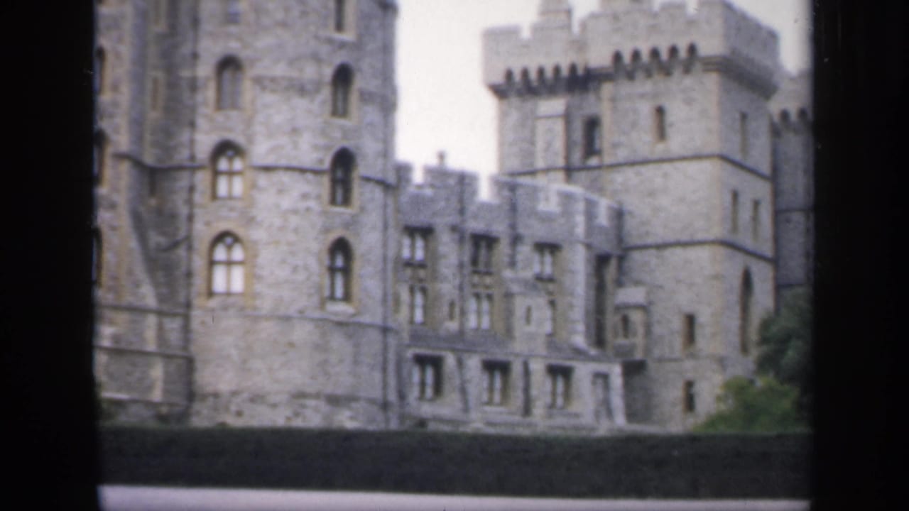 1949 England 8mm view of a grey stone castle facade with battlements, arched windows and a low dark foreground barrier.