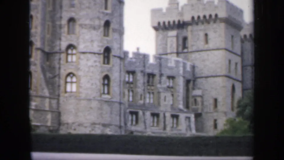 1949 England 8mm view of a grey stone castle facade with battlements, arched windows and a low dark foreground barrier.