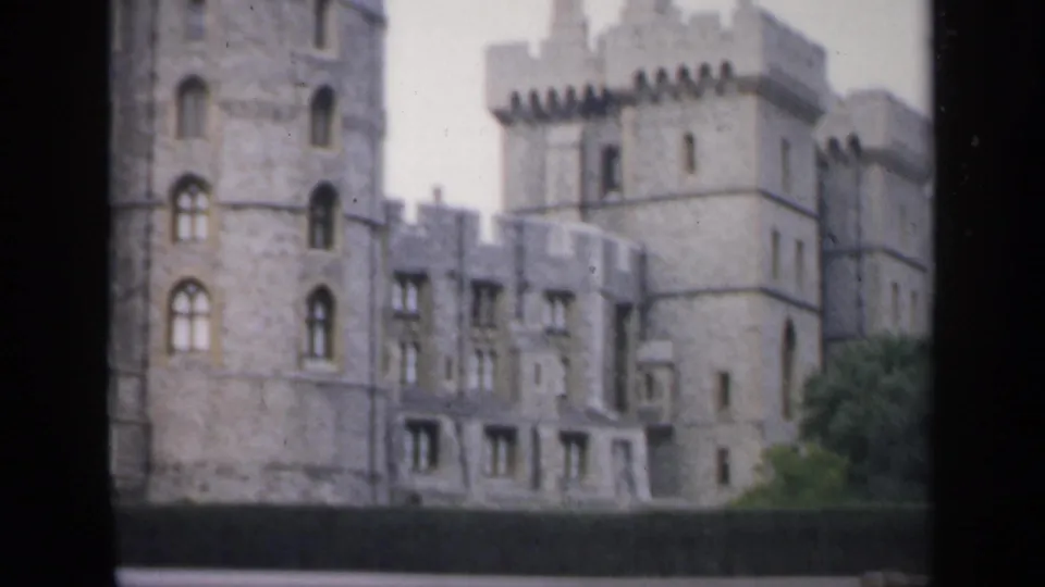 1949 England 8mm frame of the castle exterior, with grey stone walls, arched windows, battlements and soft home-movie grain.