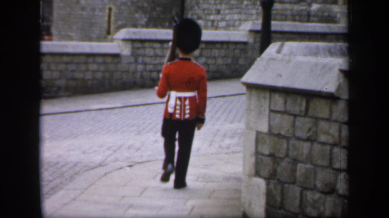 A British guard in red ceremonial uniform marches away through a stone courtyard at the Tower of London in 1949 home-movie footage.