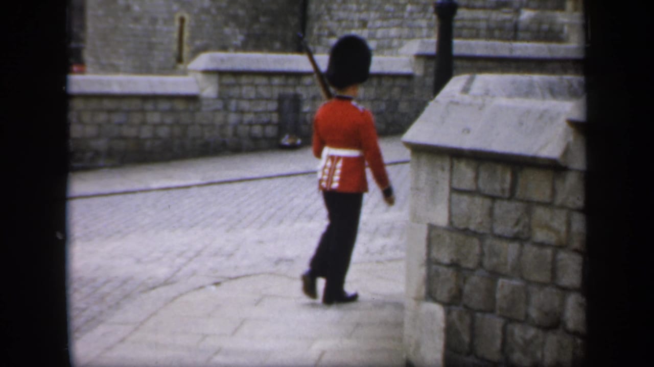 Uniformed guard turns beside a low stone wall while carrying a rifle.