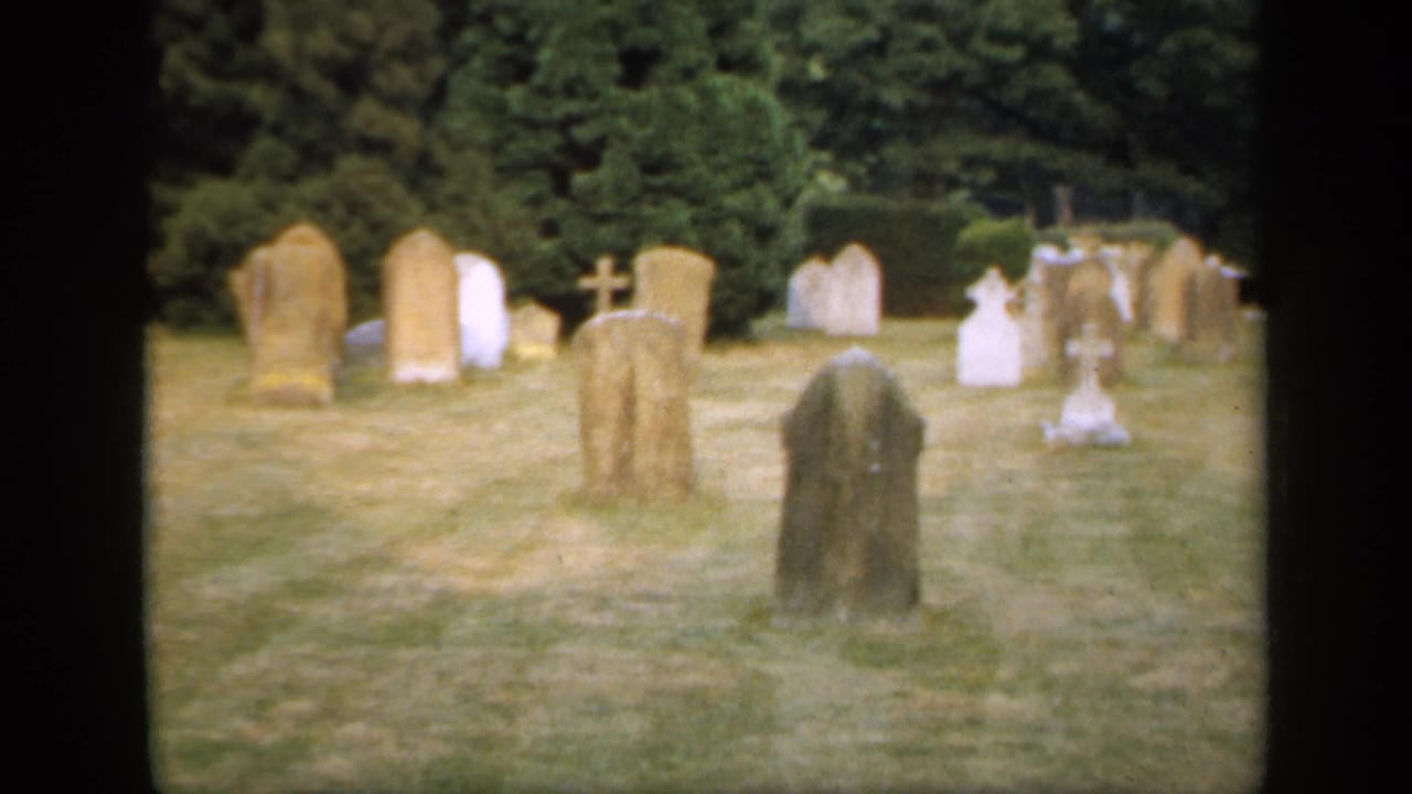 Grassy cemetery with weathered headstones and crosses framed by dark 8mm film borders.