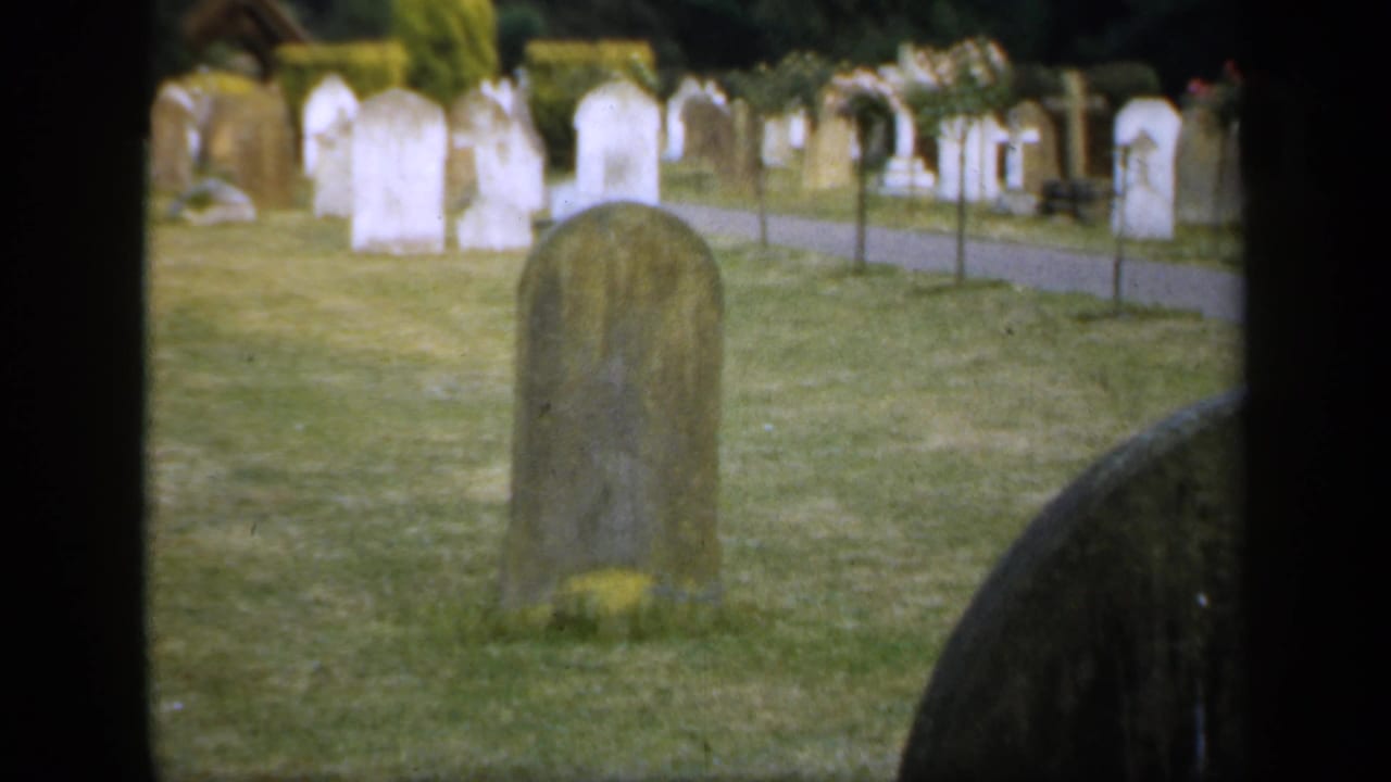Grassy churchyard with upright headstones and a path in the background.