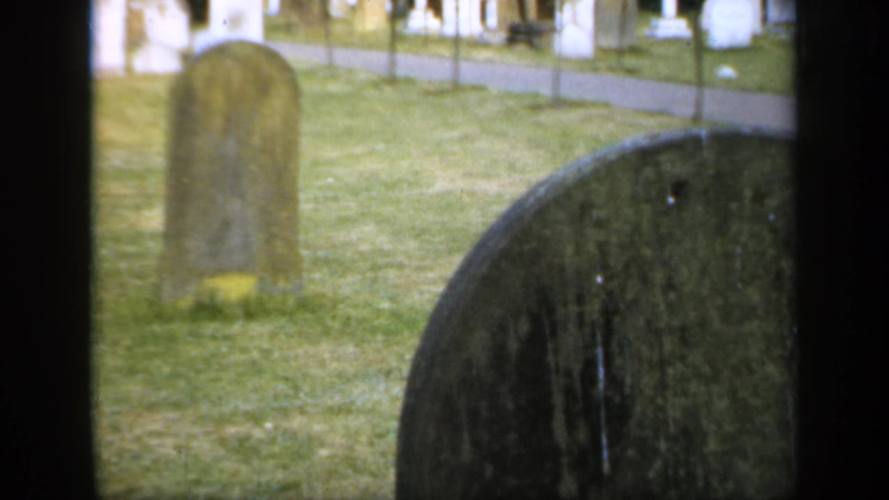 1949 England churchyard view with a rounded headstone in the grass and a larger grave marker close to the camera.