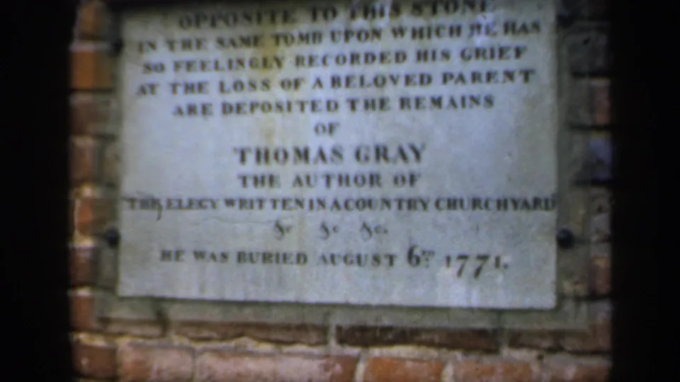 1949 England 8mm frame showing a weathered plaque commemorating Thomas Gray, with brickwork around the stone and soft film focus.