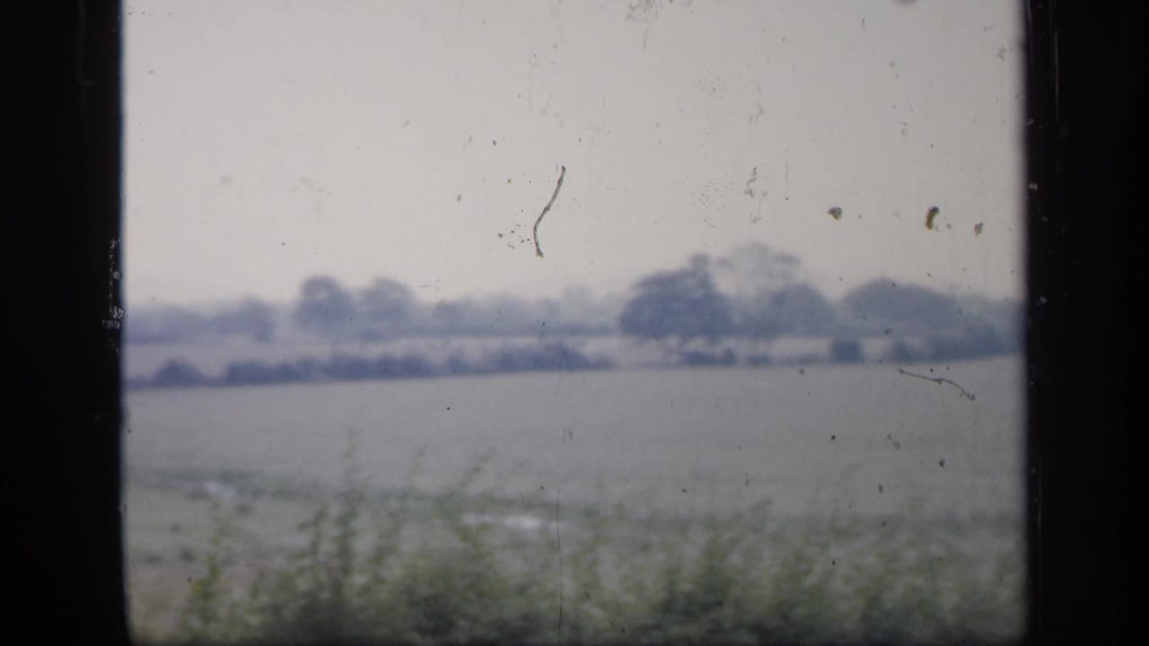 1949 England 8mm frame with a low field, distant trees, pale sky, and visible dust and scratches across the scan.