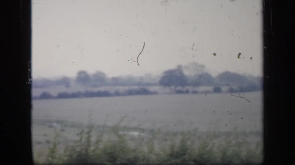 1949 England 8mm frame with a low field, distant trees, pale sky, and visible dust and scratches across the scan.