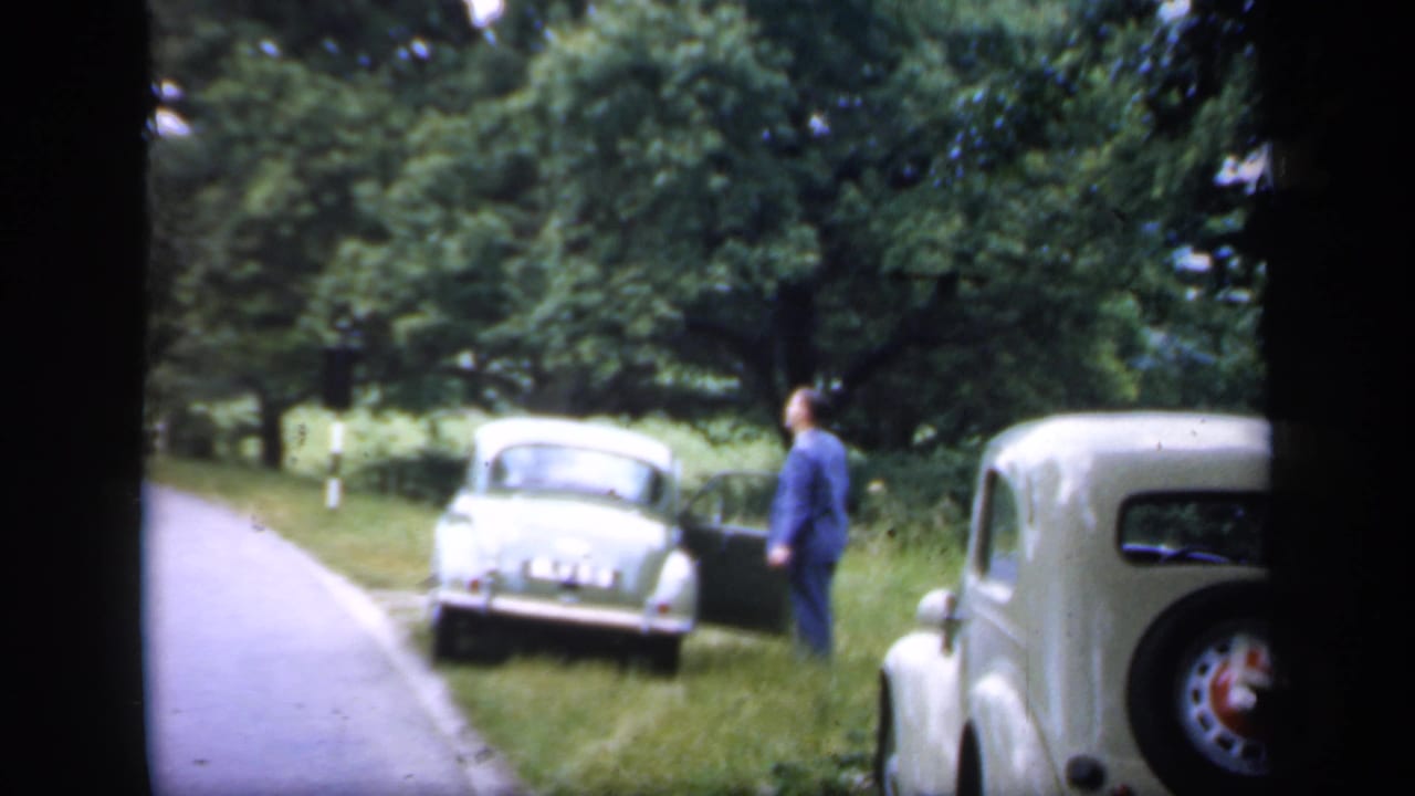 1949 England roadside frame showing two vintage cars on a grass verge, with a suited man near the nearer open door.