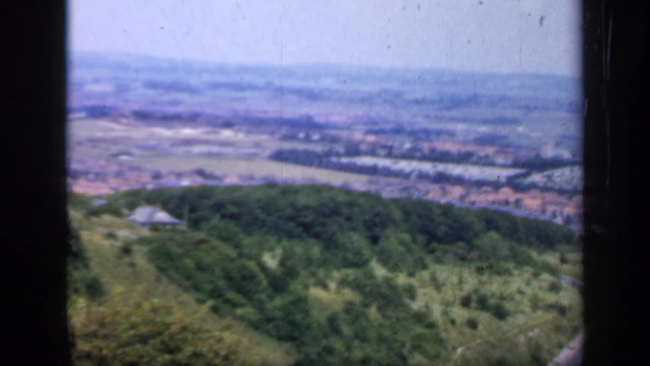 The England 1949 footage shifts to a soft, grainy hilltop panorama over a valley, town edges, fields, and wooded slopes.