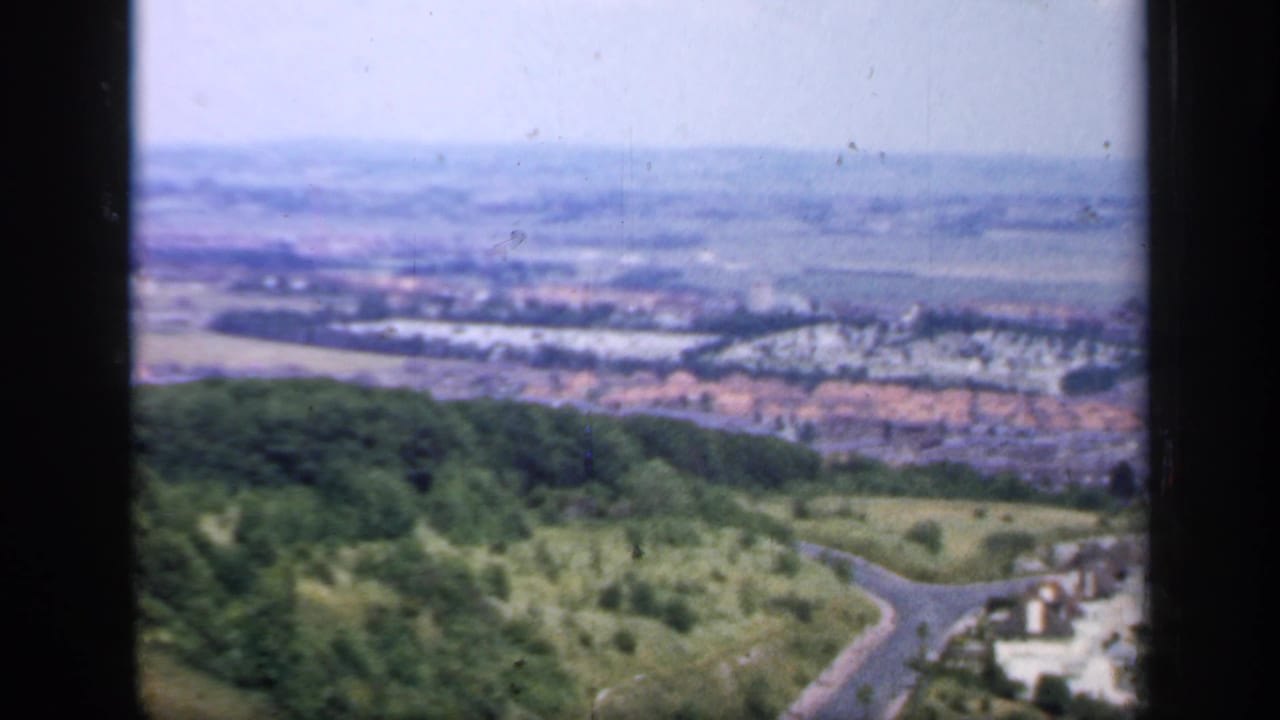 A 1949 England hilltop view shows a wooded foreground, hazy valley, scattered housing, fields, and a winding road below.