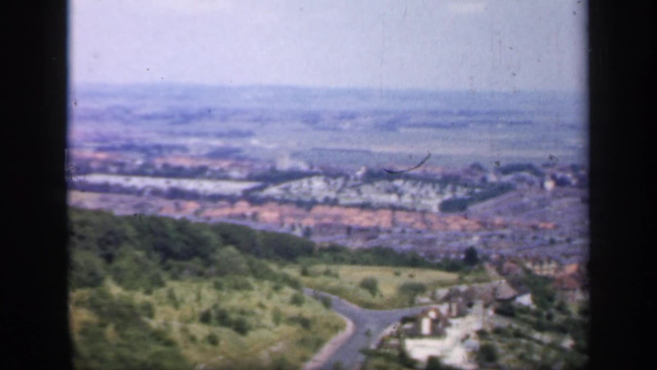 Hilltop view over a small town with roads, rooftops, trees, and open fields in the distance.