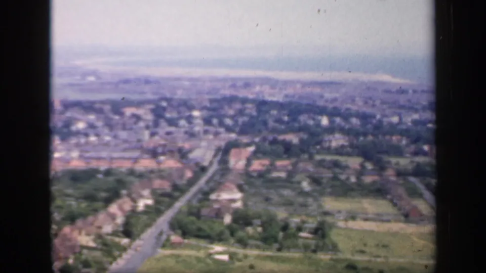 1949 England 8mm frame looking across suburban houses, a main road, trees, fields, and a hazy distant townscape.
