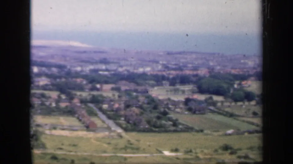 1949 England 8mm aerial frame with open farmland in front, scattered homes and roads below, and a hazy town in the distance.