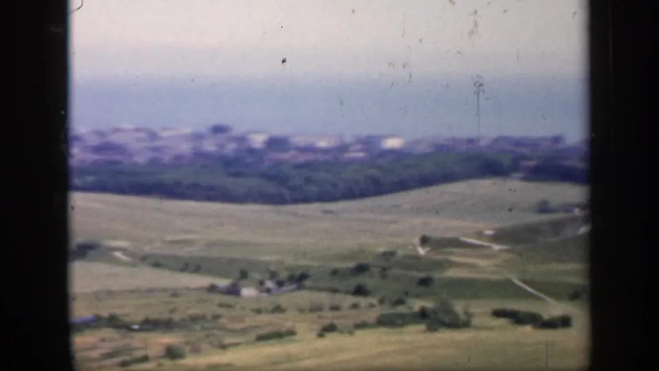 1949 England 8mm view of rolling countryside, distant town forms, scattered trees, and dark film gate edges.