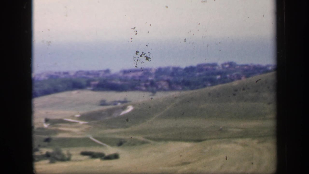 1949 England 8mm frame showing soft-focus green hills, curving tracks, scattered trees, and a distant town edge.