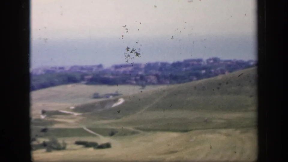 1949 England 8mm frame showing soft-focus green hills, curving tracks, scattered trees, and a distant town edge.