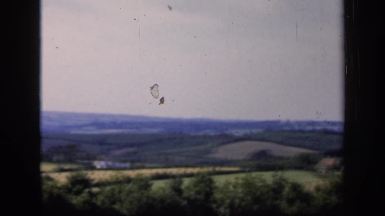 1949 8mm home-movie view of English countryside with fields, tree lines, pale sky, and dark window framing.