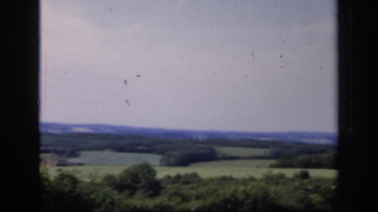 Late-1940s 8mm view of English fields and trees fading into low blue hills, with dark frame edges and visible film wear.
