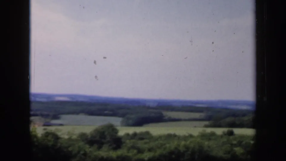Late-1940s 8mm view of English fields and trees fading into low blue hills, with dark frame edges and visible film wear.