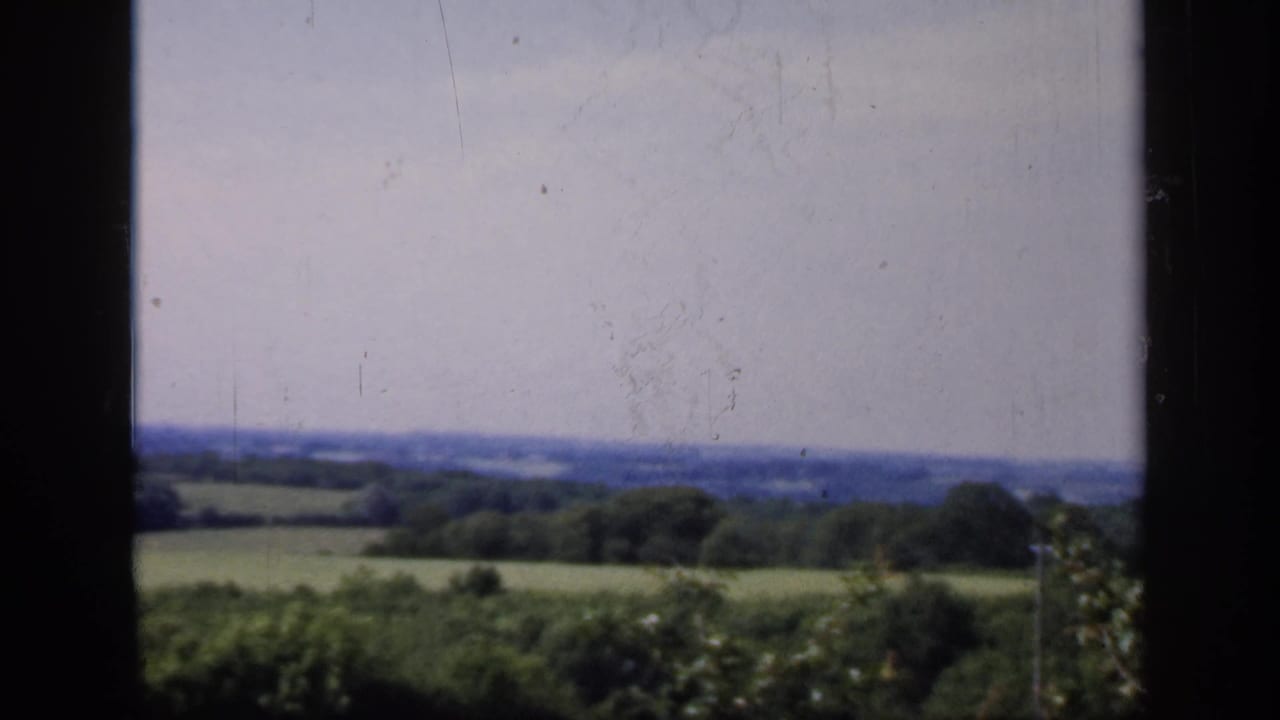 1949 England countryside remains framed by a dark mullion, with fields, hedgerows, trees, and a pale sky beyond.