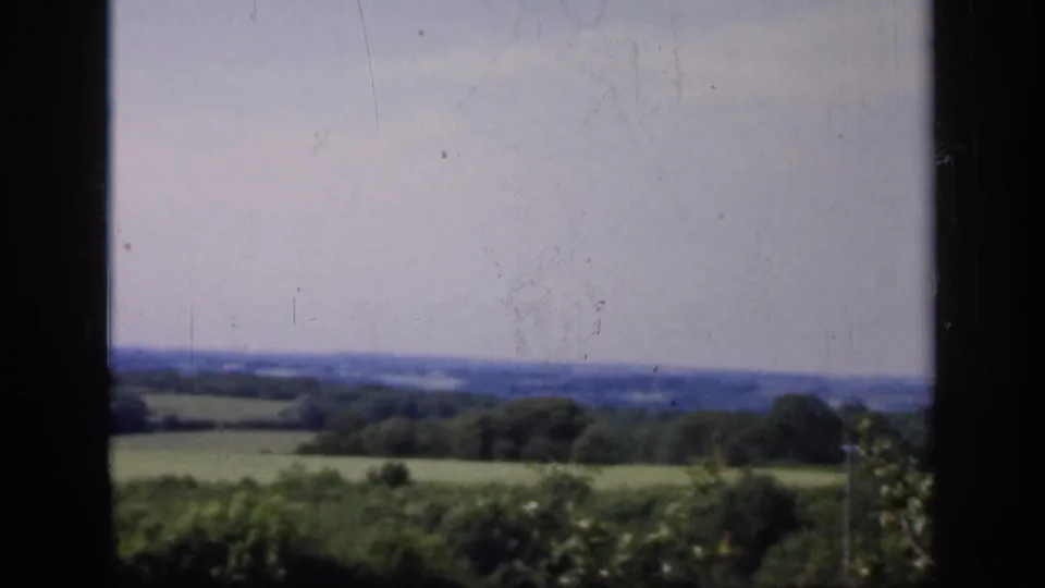 1949 England countryside remains framed by a dark mullion, with fields, hedgerows, trees, and a pale sky beyond.