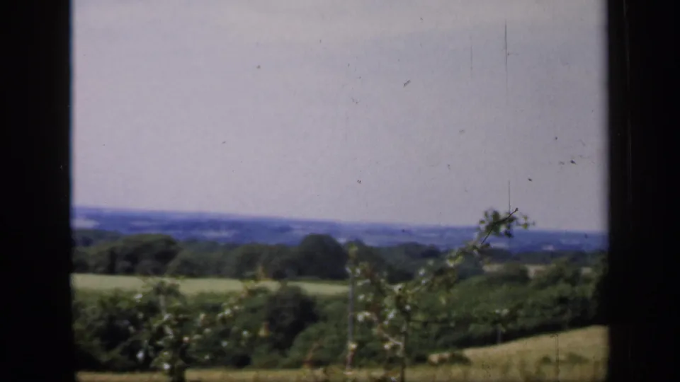 1949 England 8mm frame showing a lower angle through the window toward shrubs, open fields, trees, and a hazy horizon.