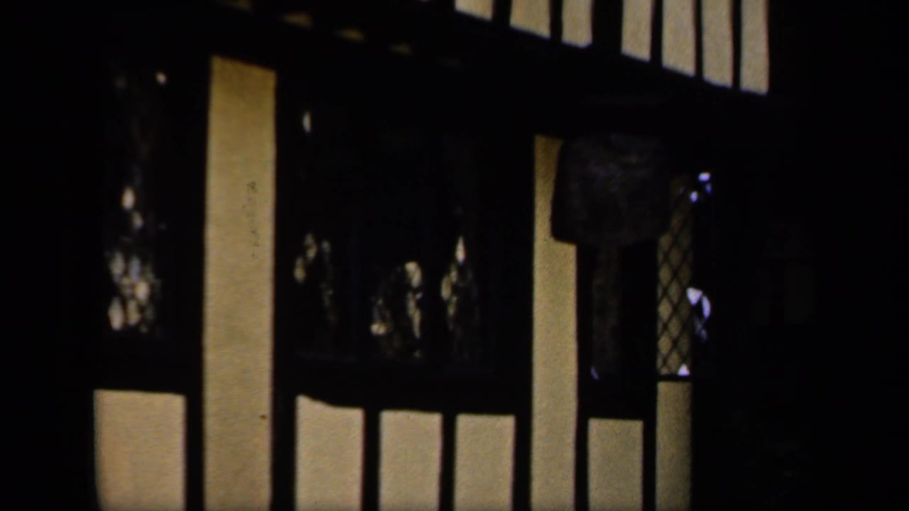 Shadowed interior frame from the 1949 England home movie, showing vertical light shapes and dark structural lines.
