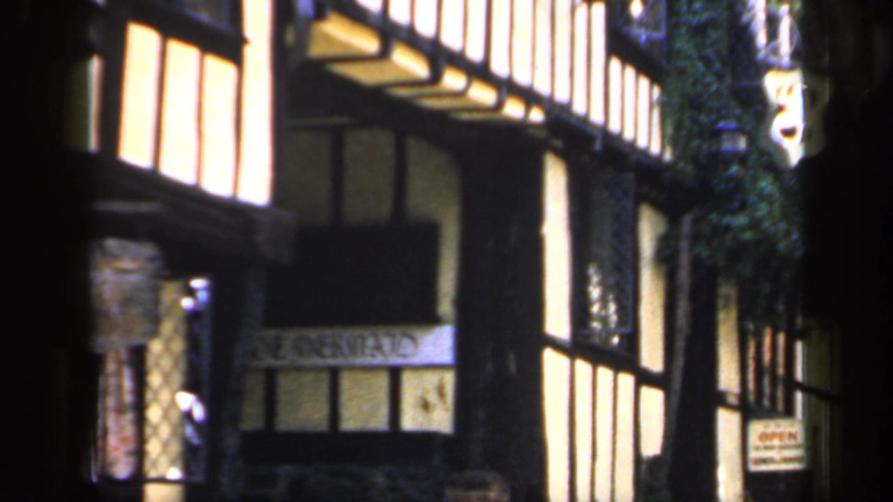 1949 England travel footage frames the building at an angle, showing timber framing, greenery, window bays, and an open sign near the lower facade.