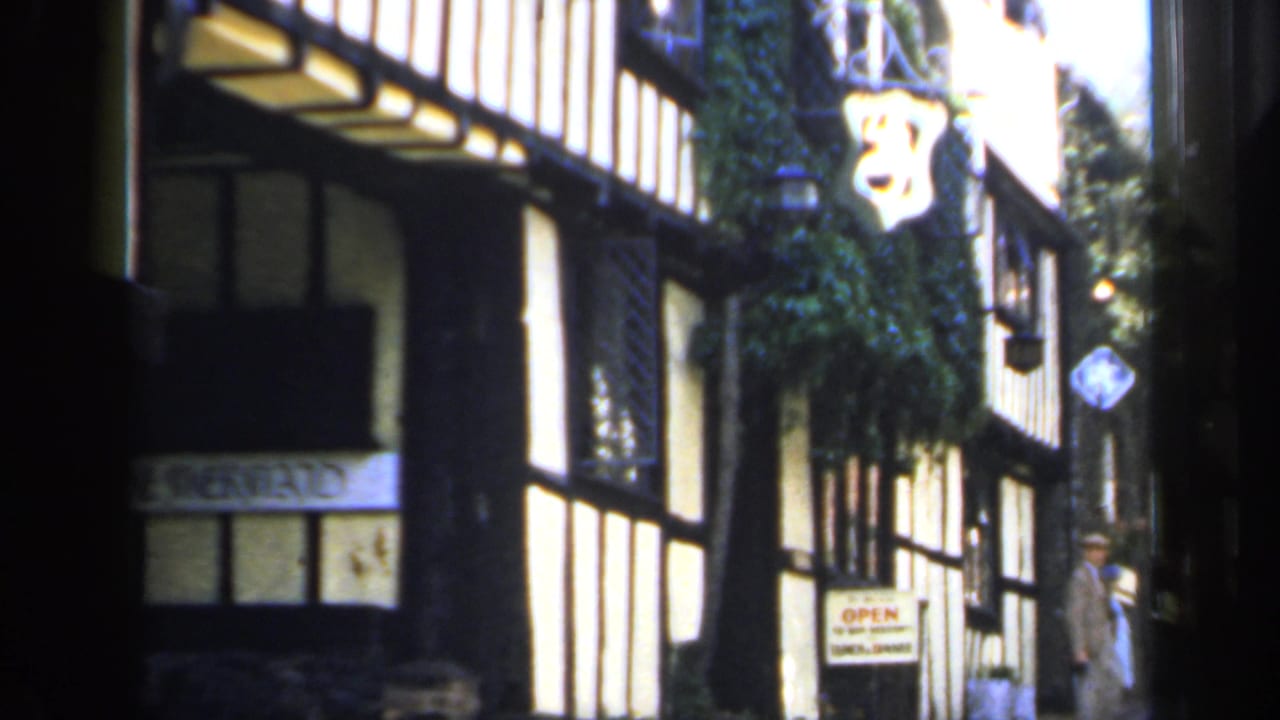 Timber-framed shopfront on a narrow street with hanging sign and shop windows.