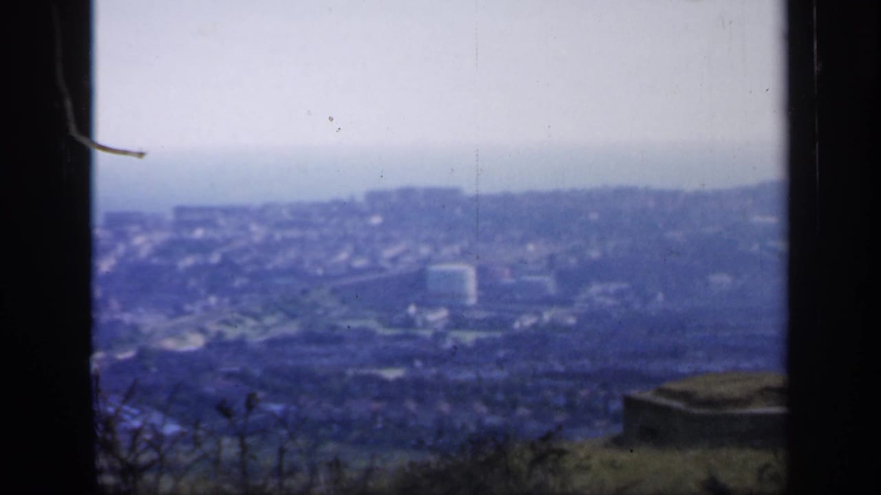 Distant coastal town viewed through dark window edges from a high hillside.