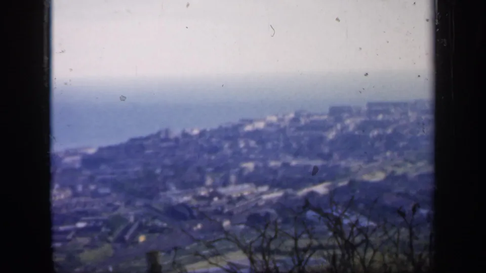 Late-1940s home-movie view over an English coastal town, with bare branches in front and sea beyond the buildings.