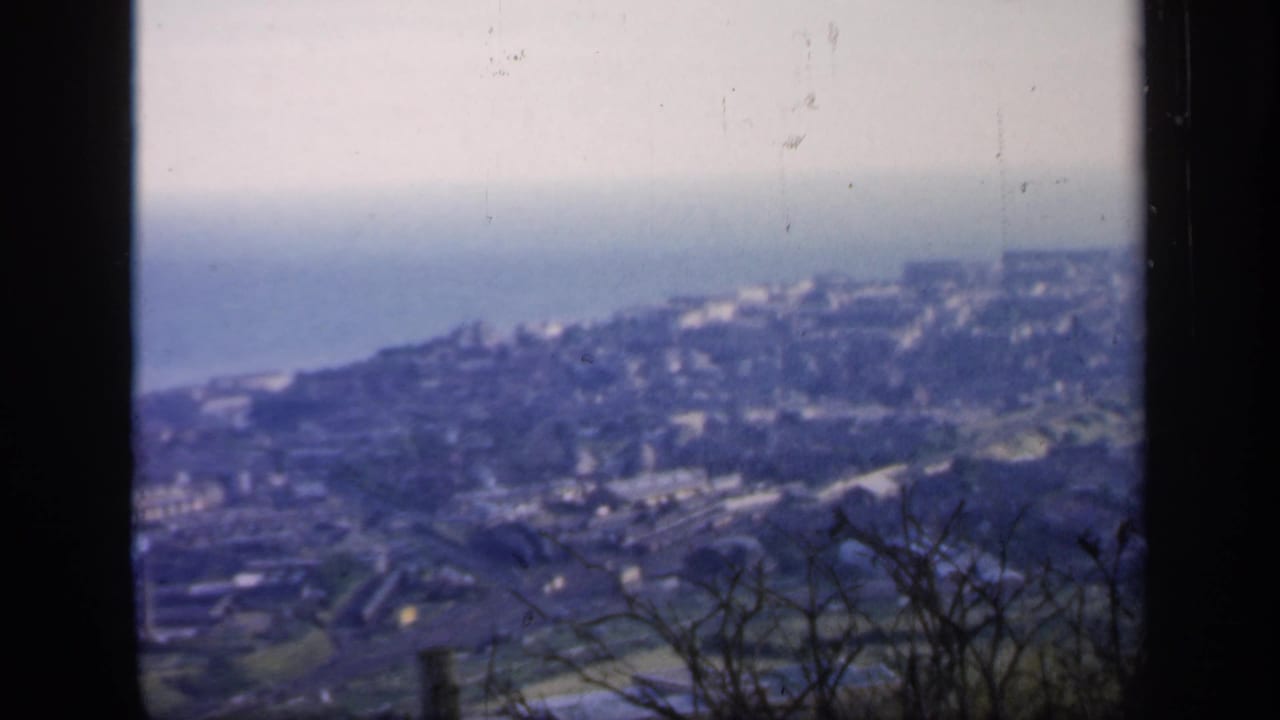 Soft distant view of a coastal hillside town and sea seen through dark frame edges.