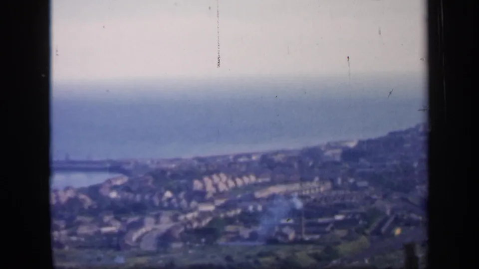 1949 England home-movie frame of a coastal town below a hazy sea horizon, seen from above.