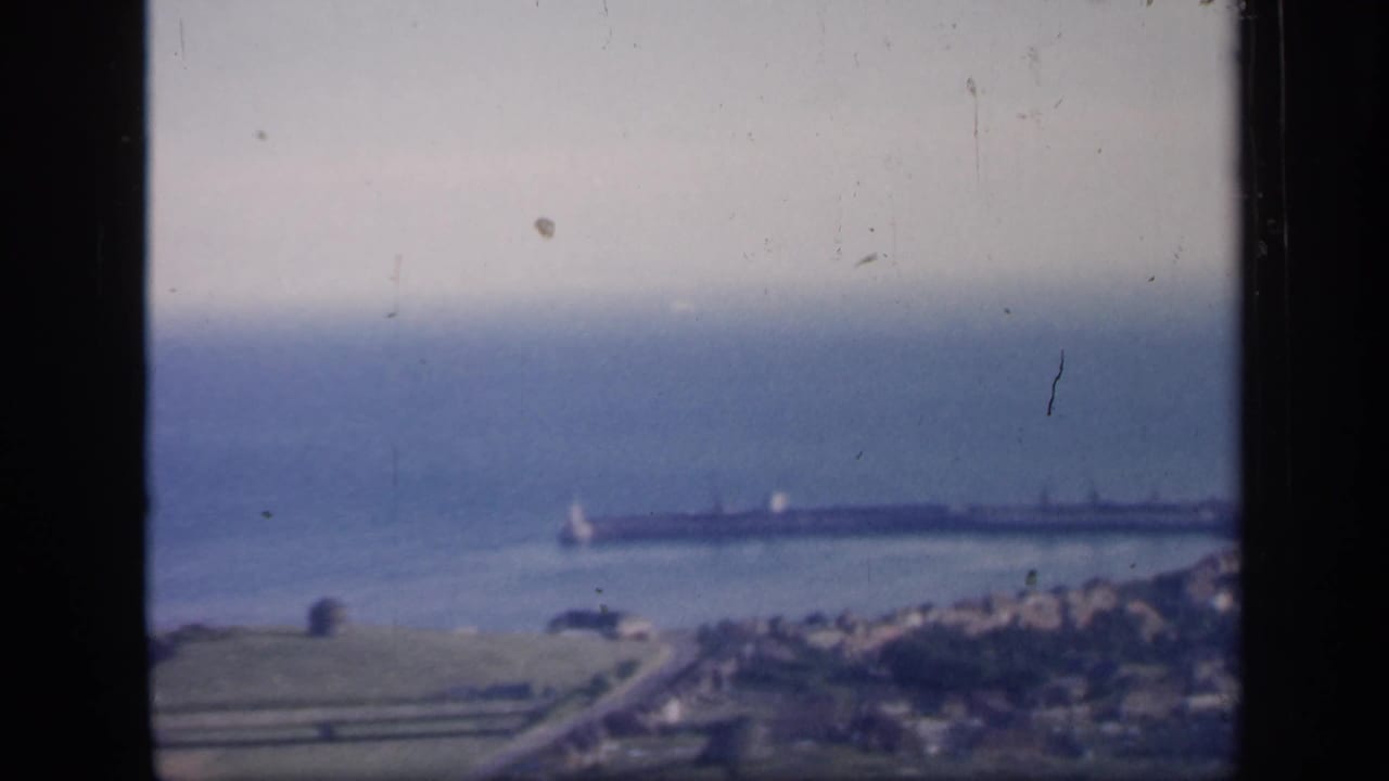 Distant coastal town and long pier seen across a bay from an elevated viewpoint.
