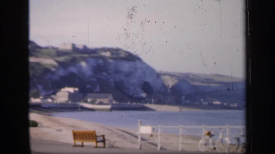Vintage England seaside frame showing chalk cliffs, harbor edge, promenade railings, benches, and bicycles.